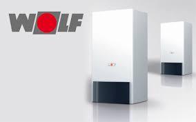 Dwa białe kotły grzewcze marki Wolf na jasnym tle, z widocznym logo producenta w lewym górnym rogu. Jeden kocioł ustawiony bliżej, drugi w oddali, oba z ciemnymi dolnymi panelami.