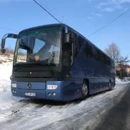 Niebieski autokar Mercedes-Benz z numerem rejestracyjnym KRA 4912N zaparkowany na ośnieżonej drodze w zimowy dzień.