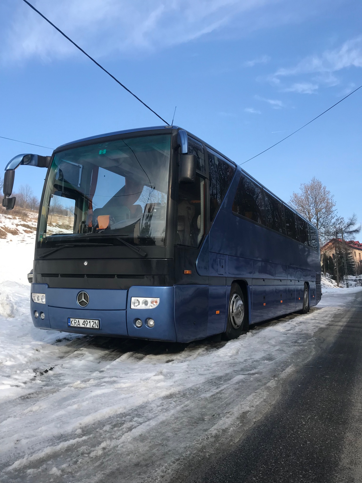 Niebieski autokar Mercedes-Benz z numerem rejestracyjnym KRA 4912N zaparkowany na ośnieżonej drodze w zimowy dzień.
