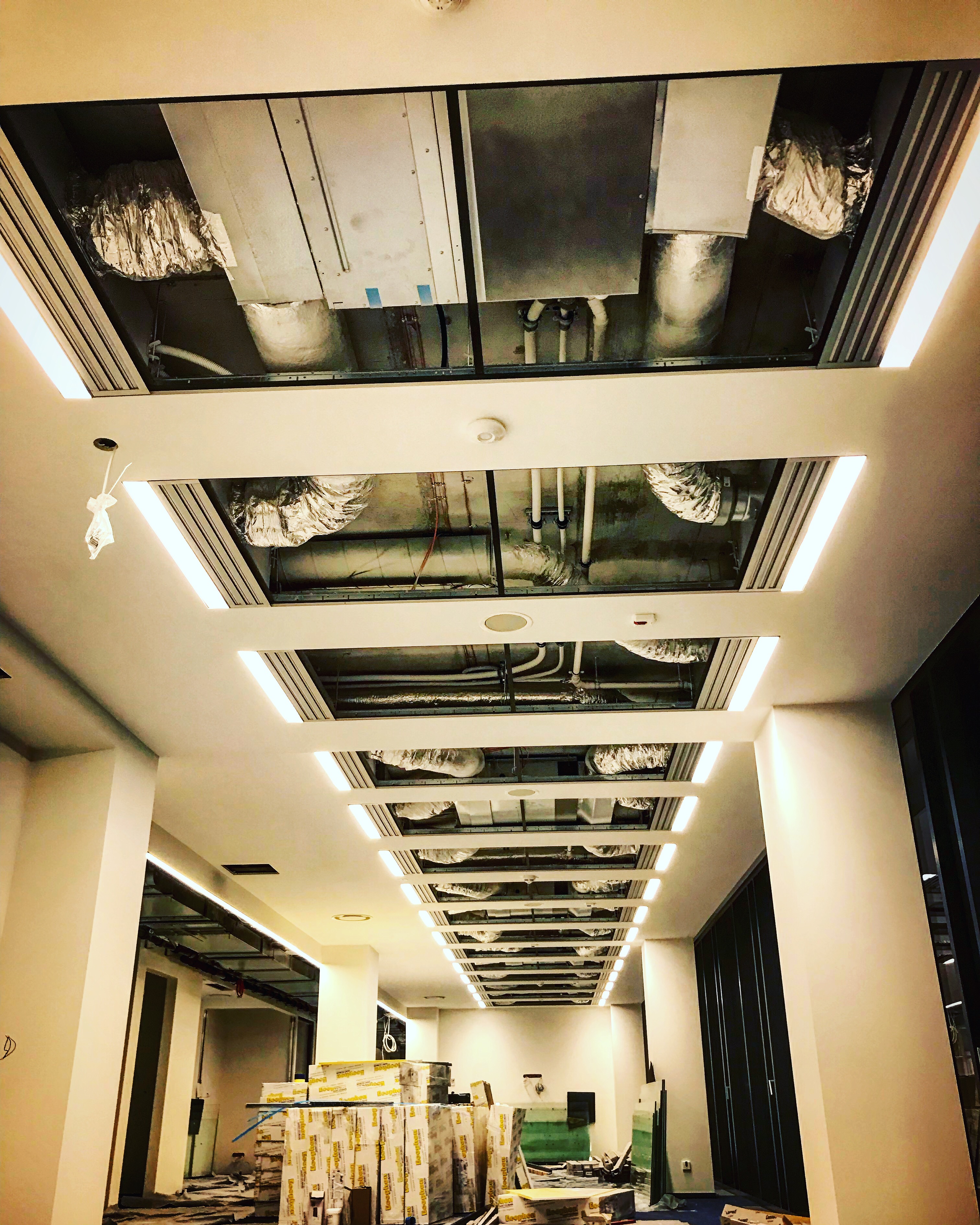 Sufit podwieszany z widocznymi instalacjami wentylacyjnymi i oświetleniem LED w nowym budynku, widok z dołu, w tle materiały budowlane.