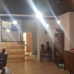 Wnętrze salonu fryzjerskiego w stylu retro z drewnianą ladą, fotelami fryzjerskimi, umywalkami, wiszącymi lampami, dekoracjami ściennymi i meblami w stylu vintage.