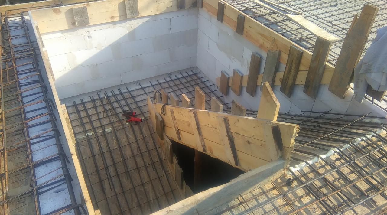 Zbrojenie fundamentów domu z bloczków, widoczne drewniane szalunki i siatka zbrojeniowa, czerwone narzędzie leży na zbrojeniu.