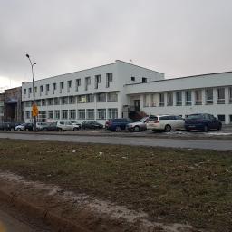 S-Stone Sylwester Andrzejczak - Biały budynek z płaskim dachem w Warszawie, widoczny z ulicy, z zaparkowanymi samochodami i fragmentem trawnika, częściowo w trakcie remontu z widocznymi rusztowaniami.