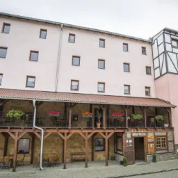 Fasada budynku z napisem 'Restauracja' pionowo z boku, balkon z drewnianą konstrukcją i kwiatami, oraz wejście do 'Zamkowy Młyn'.