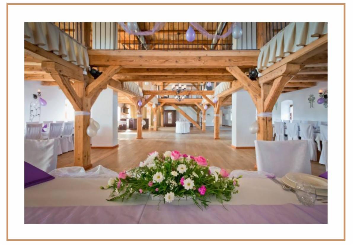 Uroczysta sala weselna z drewnianą konstrukcją stropu i kolumnami, udekorowana balonami i kwiatami na stole prezydialnym, przygotowana na przyjęcie.