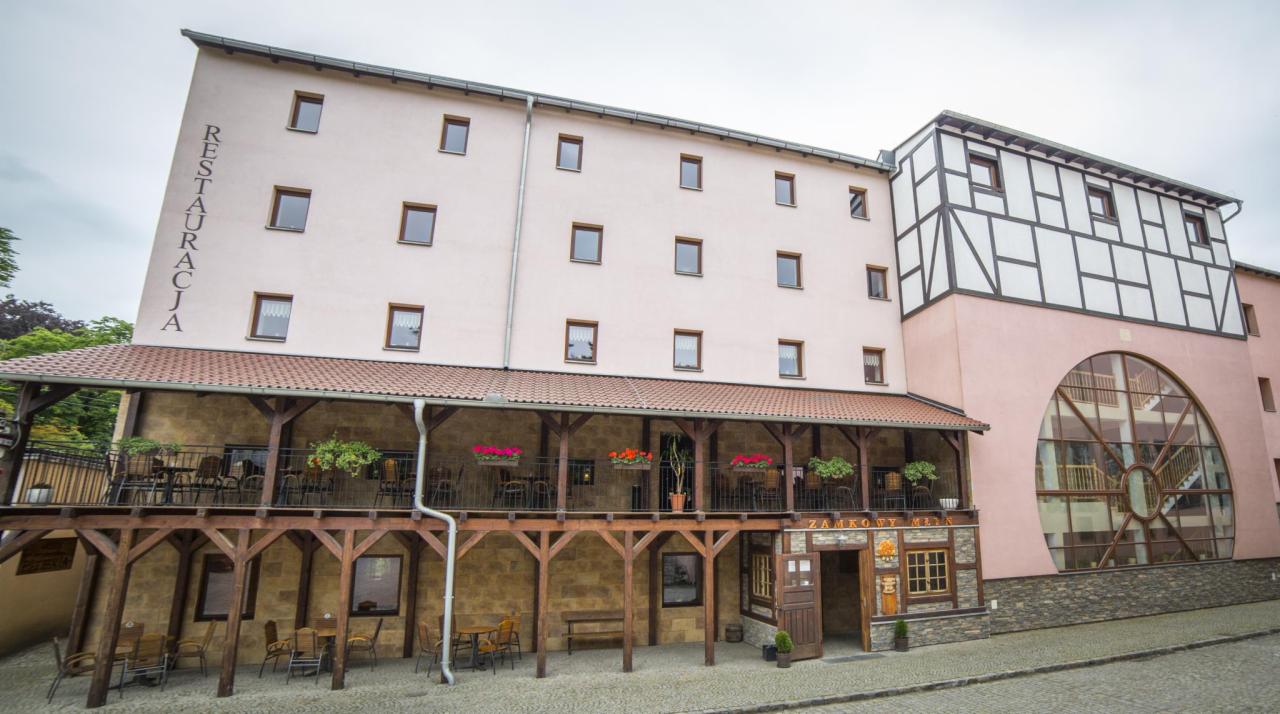 Fasada budynku z napisem 'Restauracja' pionowo z boku, balkon z drewnianą konstrukcją i kwiatami, oraz wejście do 'Zamkowy Młyn'.