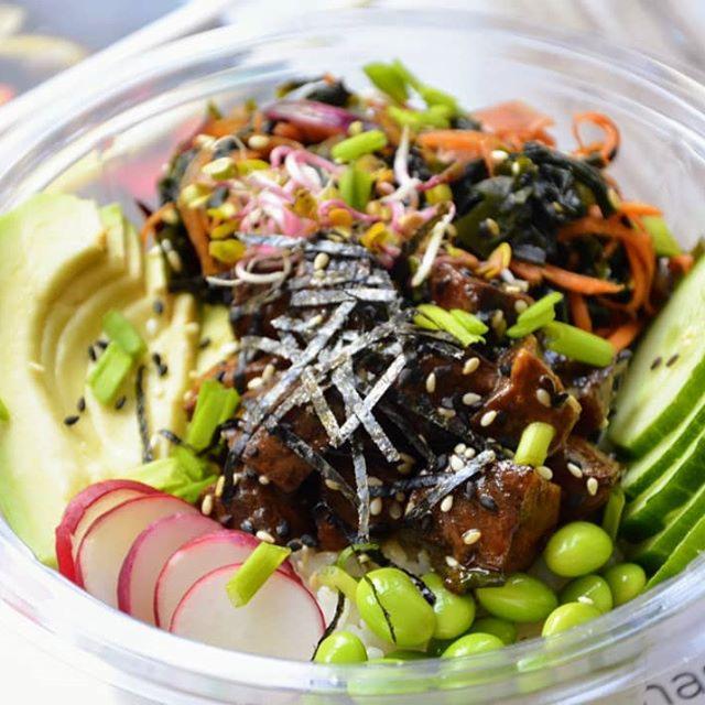 Poke bowl w przezroczystej misce z awokado, rzodkiewką, ogórkiem, edamame, wodorostami, marchewką i kiełkami, posypane sezamem.