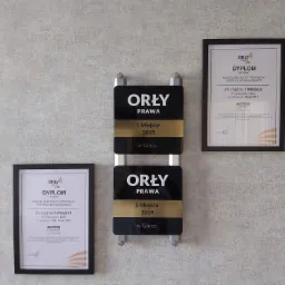 Tablica z nagrodami Orły Prawa za lata 2018 i 2019 obok dyplomów w ramkach na ścianie w Kancelarii Radcy Prawnego Patrycjusza Miłaszewicza w Górze.