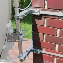 Szczeg&oacute;łowe ujęcie mocowania anteny satelitarnej do ściany z czerwonej cegły, widoczne metalowe wsporniki i śruby mocujące.