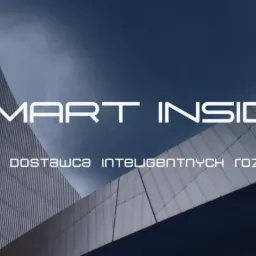 Elewacja nowoczesnego budynku biurowego z napisem 'SMART INSIDE, Twój dostawca inteligentnych rozwiązań' na tle pochmurnego nieba.