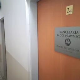 Tabliczka informacyjna Kancelarii Radcy Prawnego Daniel Krysztoforski, umieszczona na brązowych drzwiach z numerem 2a, widoczna z korytarza.