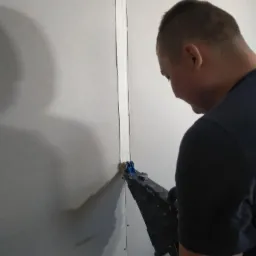 Pracownik szpachluje łączenie płyt karton-gips przy użyciu specjalistycznego aplikatora z rolkami.