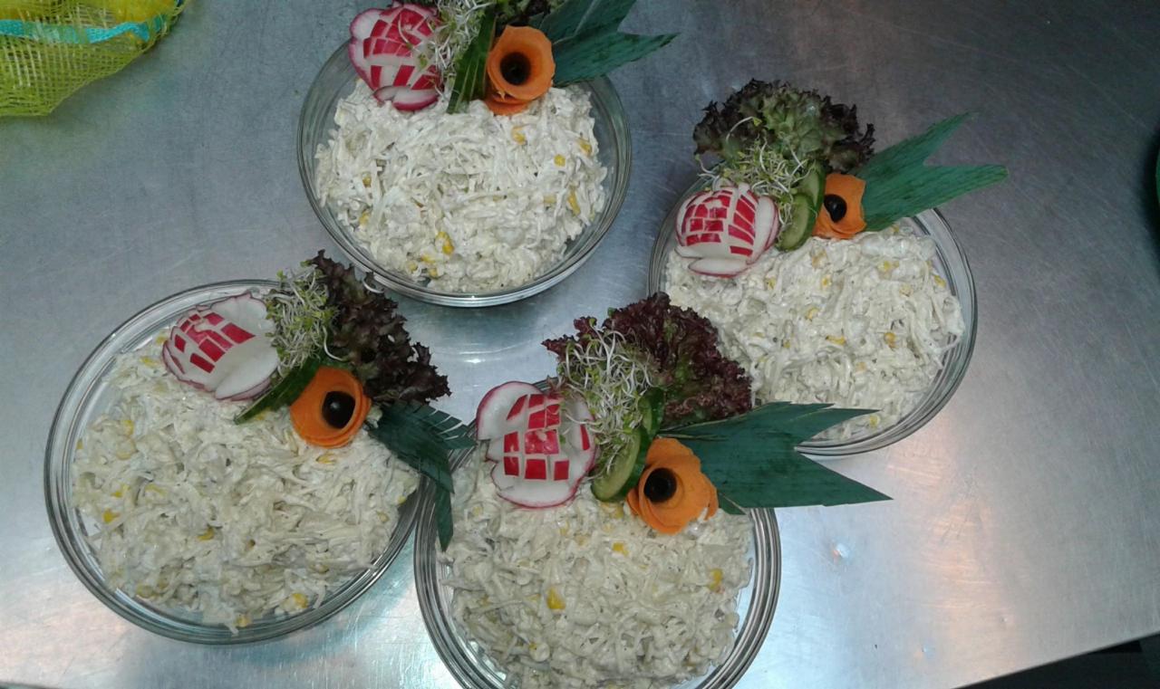 Cztery szklane miseczki z sałatką jarzynową, udekorowane rzodkiewką z wyciętymi kwadratami, marchewkowym kwiatkiem i zieleniną, ustawione na metalowym stole.