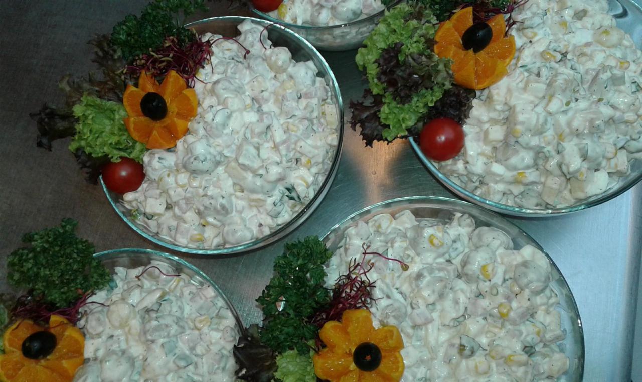 Szklane miski z sałatką jarzynową udekorowane pomidorkiem cherry, plastrami pomarańczy w kształcie kwiatów i zieloną pietruszką na metalowym blacie.