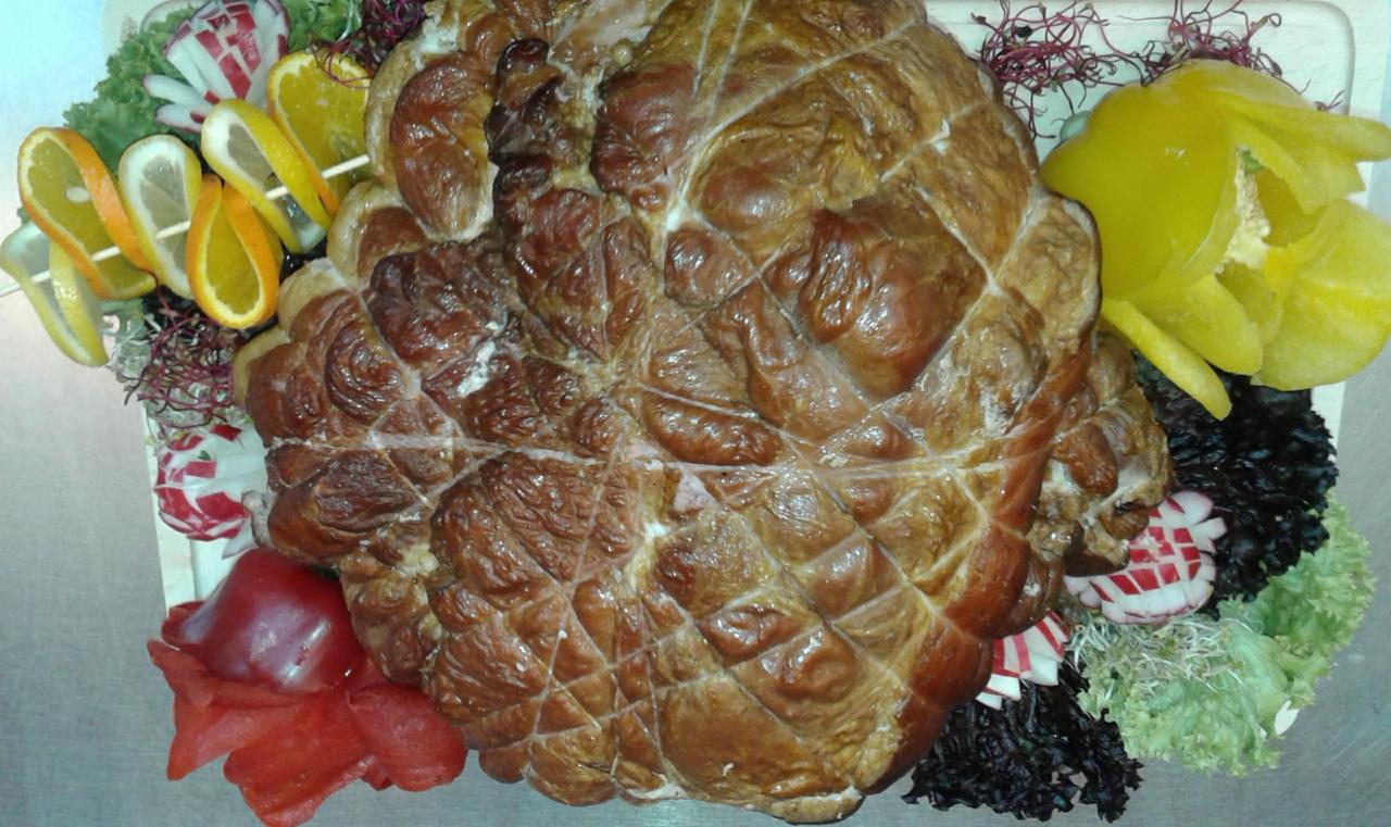 Wędzonka w siatce wędliniarskiej, udekorowana plasterkami pomarańczy i cytryny na szpadce, rzodkiewkami, papryką i sałatą na desce.