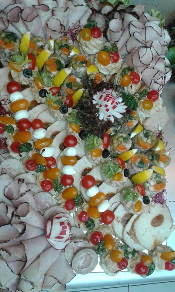 Dekoracyjna taca z przekąskami: wędliny, koreczki z pomidorkami i mozzarellą, galaretki z warzywami, ozdobiona rzodkiewką.