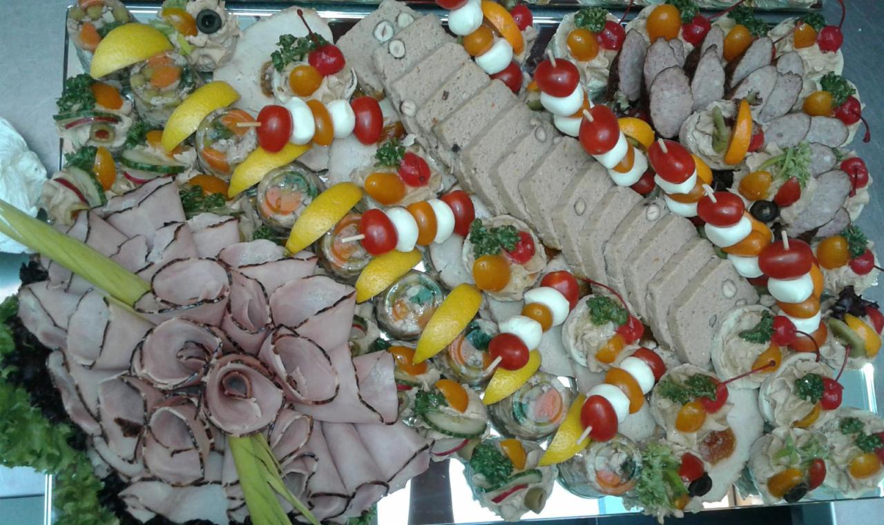 Dekoracyjna taca z różnorodnymi przekąskami: roladki z szynki, pasztet w plastrach, szaszłyki z pomidorków i mozzarelli, galaretki z warzywami, ozdobione cytryną i zieleniną.