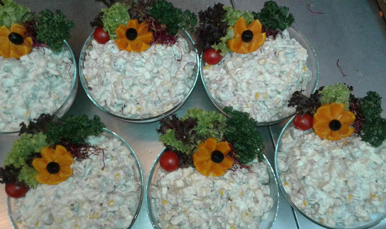 Szklane miski z sałatką, udekorowane pomidorkami cherry, sałatą i kwiatami z pomarańczy z oliwką na środku, przygotowane do serwowania.