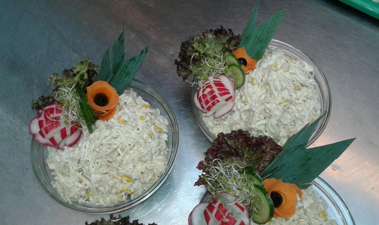 Trzy szklane miski z sałatką jarzynową, dekorowane rzodkiewką, ogórkiem, marchewką i zieleniną, ułożone na metalowym blacie.