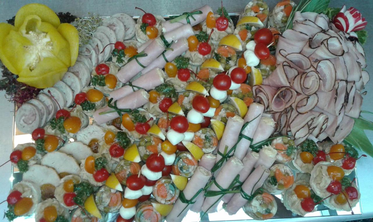 Dekoracyjna taca z zimnymi przekąskami: roladki z szynki spięte szczypiorkiem, galaretki z warzywami i plasterkami cytryny, wędliny w plastrach, pomidorki koktajlowe i żółta papryka w kształcie...