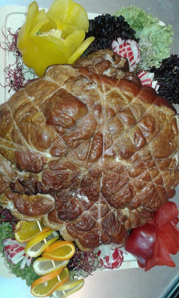 Wędzonka w siatce, otoczona dekoracją z warzyw i owoców: papryka żółta uformowana w kwiat, plasterki pomarańczy i cytryny na patyczkach, rzodkiewki, sałata.