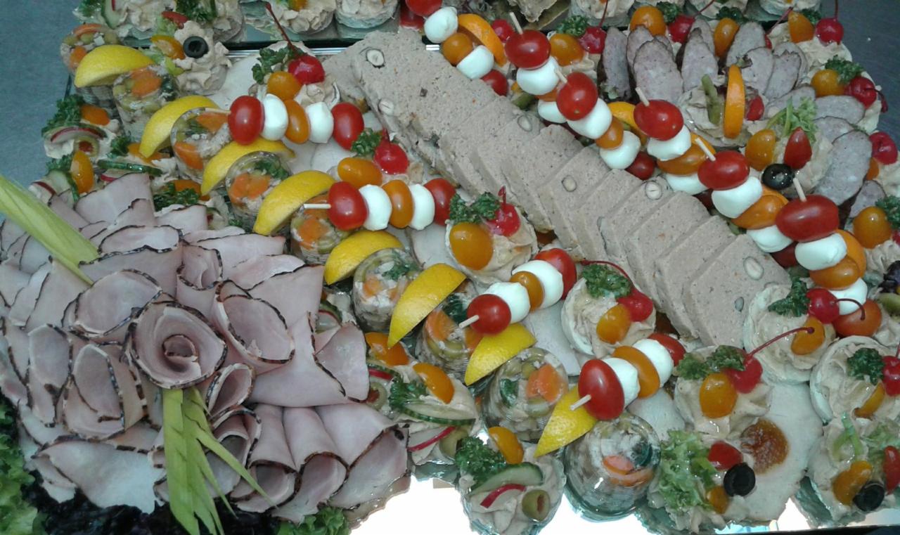 Dekoracyjny półmisek z wędlinami, pasztetem w plastrach, koreczkami z pomidorków koktajlowych i mini mozzarelli oraz galaretkami z warzywami i cytryną, ułożony na lustrzanej tacy.