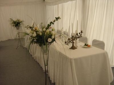 Dekoracja stołu z kwiatami w wysokich wazonach i świecznikiem na białym obrusie, tło z białych zasłon