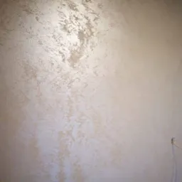 Ściana pokryta dekoracyjną, beżowo-złotą gładzią z efektem perłowym, widoczny przewód wystający ze ściany w prawym dolnym rogu.