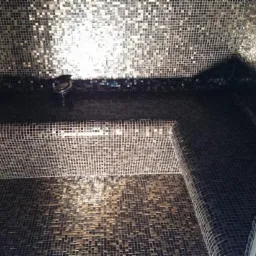 Mozaika w odcieniach brązu i złota pokrywająca ściany, sufit i siedzisko w kabinie prysznicowej, z widoczną deszczownicą i nowoczesną ramą.