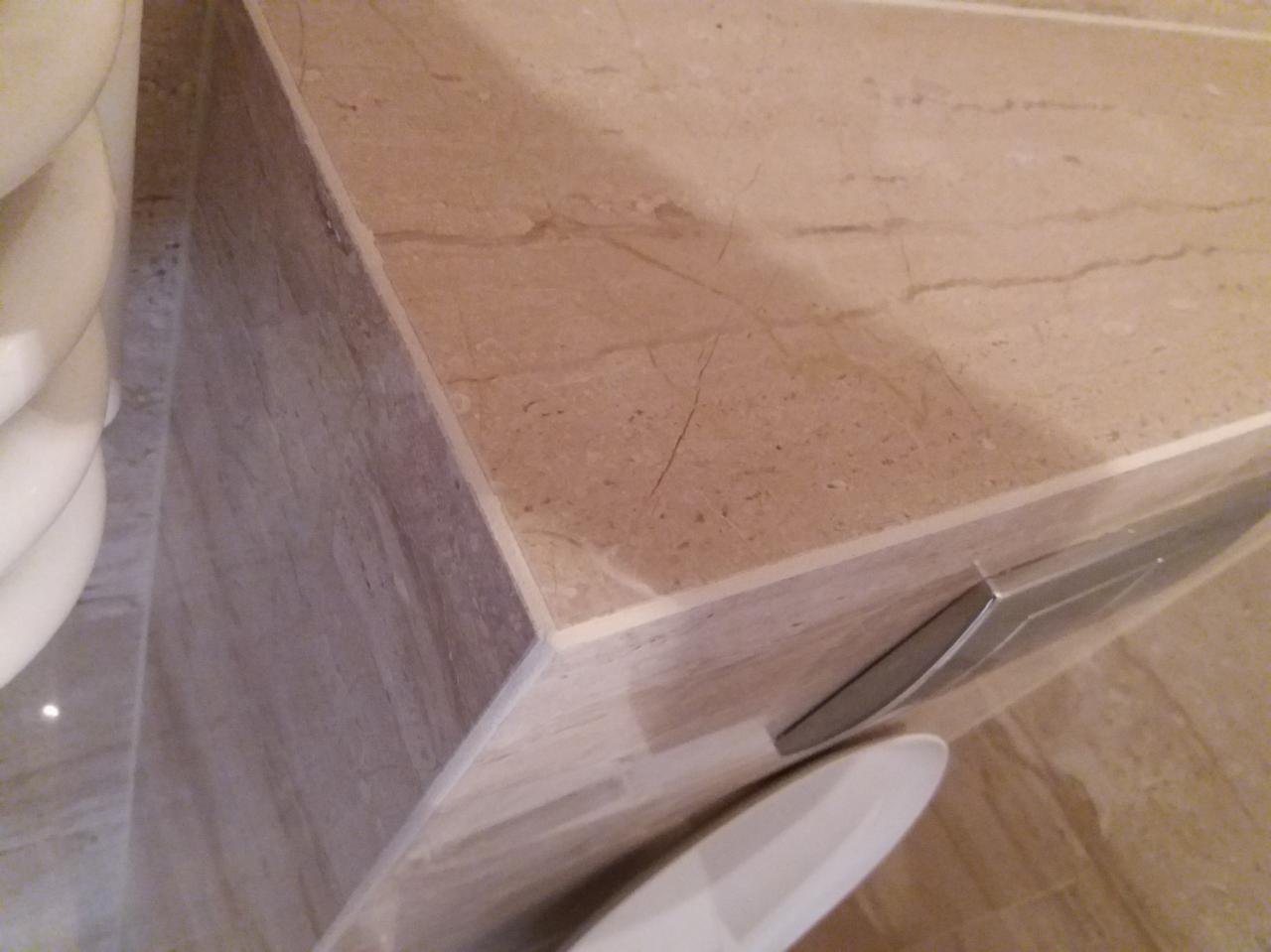 Beżowa marmurowa zabudowa toalety z widocznymi fugami i fragmentem miski ustępowej.