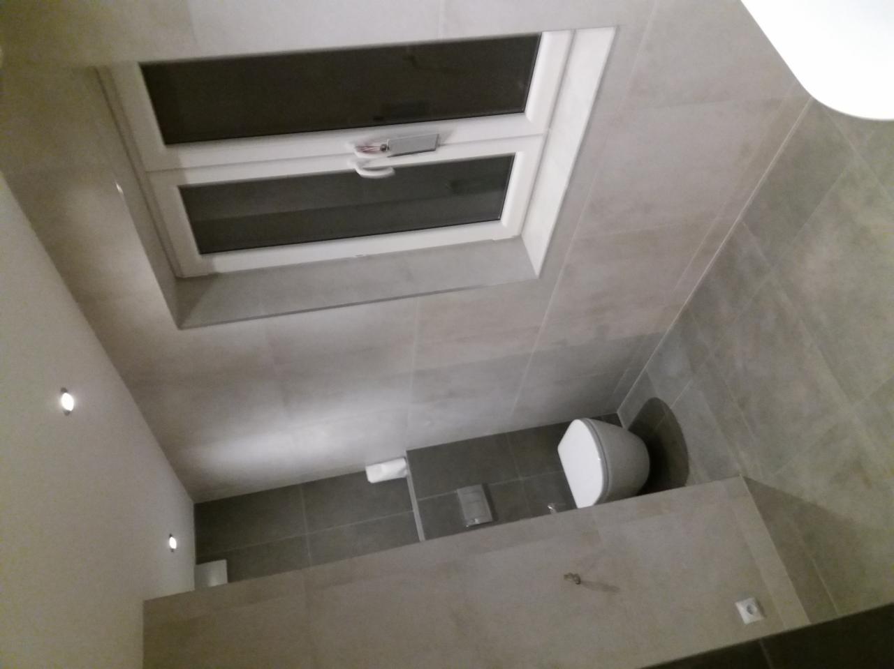 Wykończona łazienka z szarymi płytkami, oświetleniem punktowym i oknem dachowym, widok z góry.