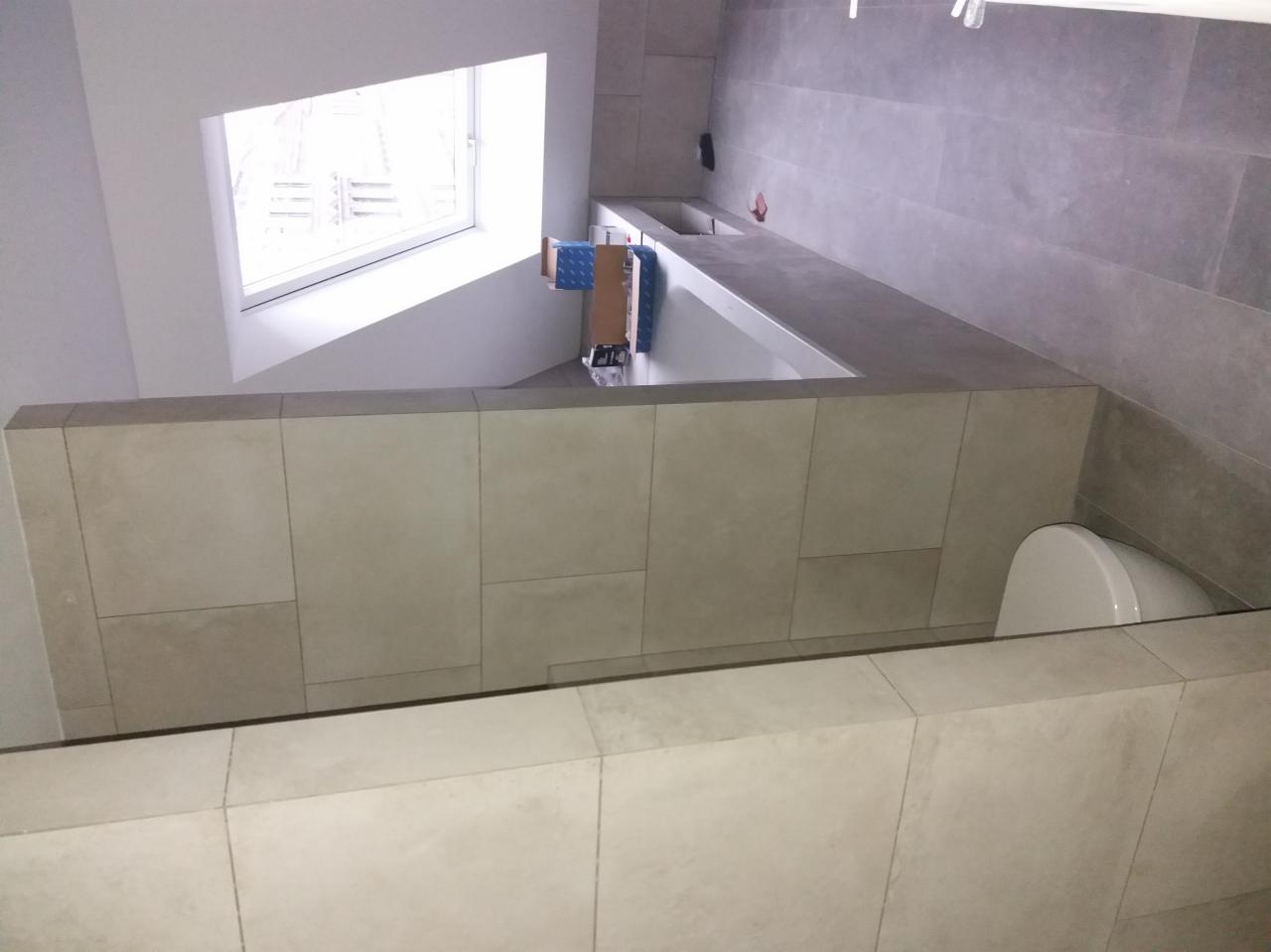 Wykończona łazienka z beżowymi i szarymi płytkami, zabudowa z umywalką i toaletą, widok z góry z perspektywy okna.