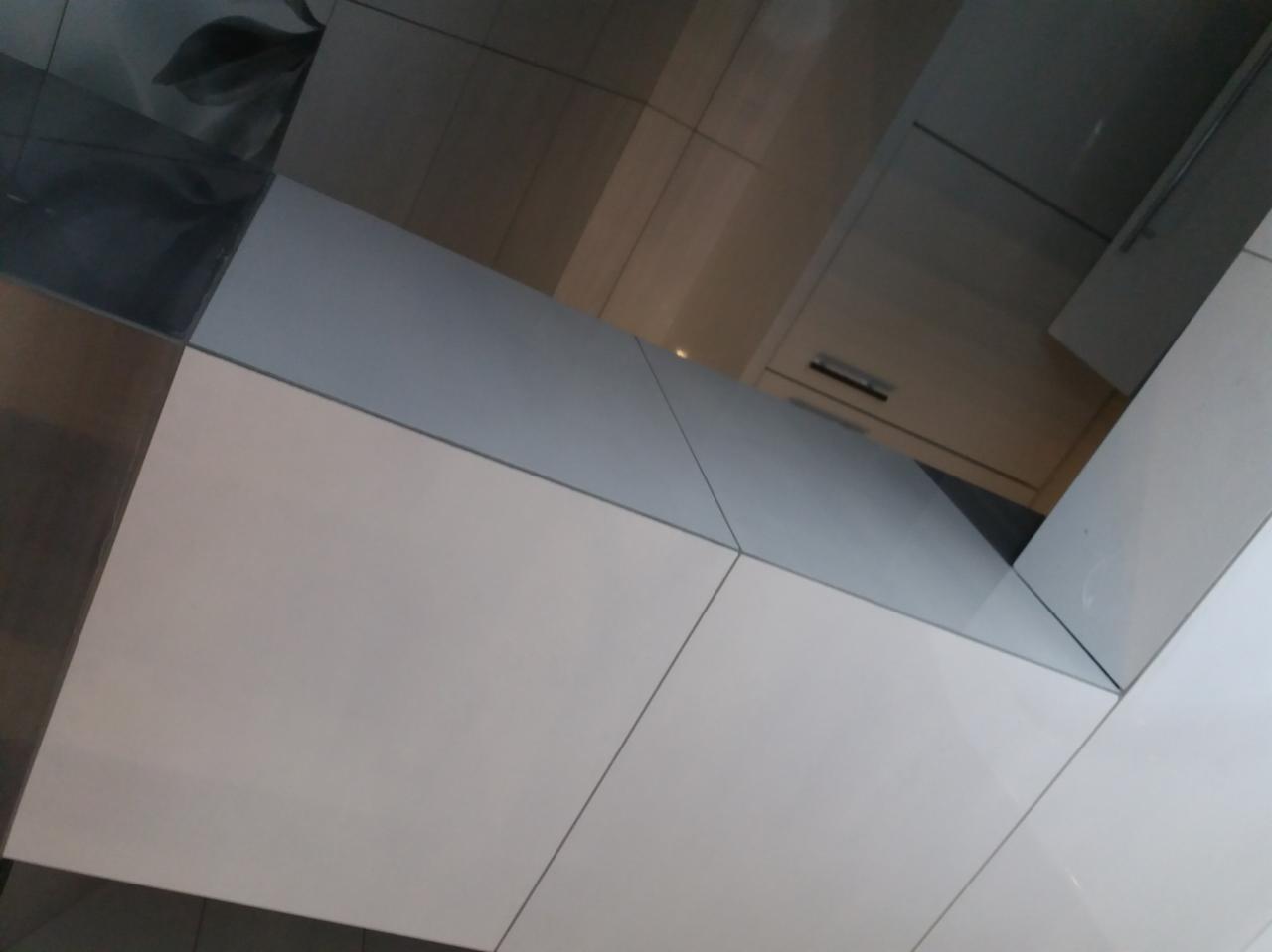 Białe, błyszczące płytki ścienne ułożone pod kątem, z widocznymi fugami i refleksami światła na powierzchni, tworzące nowoczesny wzór.