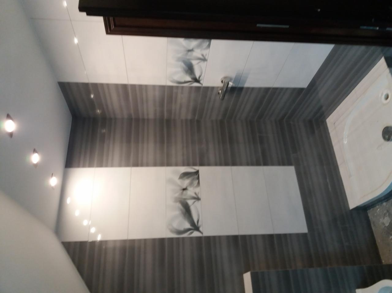 Wykończona łazienka z szarymi i białymi płytkami, dekoracyjnym motywem kwiatowym, oświetleniem punktowym sufitowym i kabiną prysznicową w rogu.