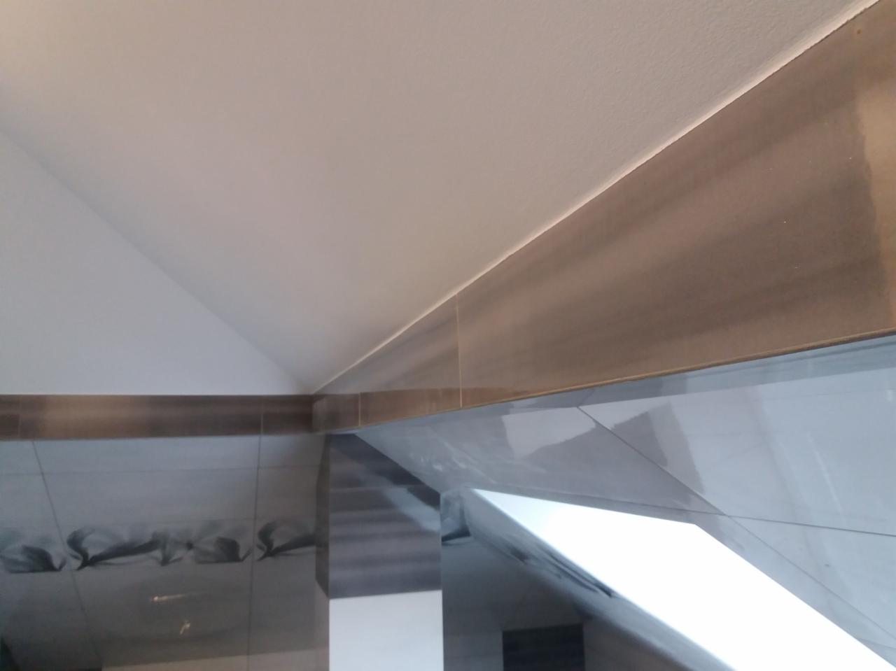 Wykończony fragment łazienki na poddaszu z szarymi płytkami, widoczne skosy sufitu i okno dachowe.