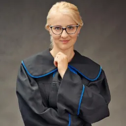 Portret kobiety w todze prawniczej z niebieskimi lamówkami, w okularach, z delikatnym uśmiechem, na neutralnym tle, Poznań.