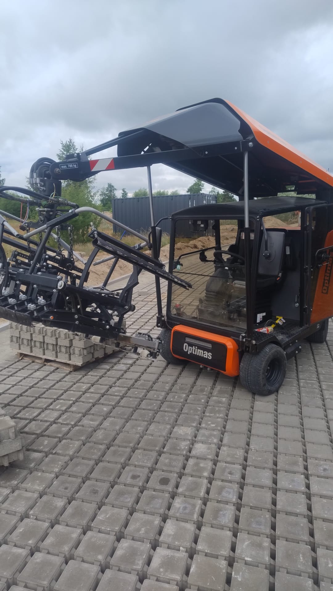 Maszyna Optimas do układania kostki brukowej na placu budowy. Widoczne ułożone kostki i paleta z kostką. Sprzęt budowlany w trakcie pracy.