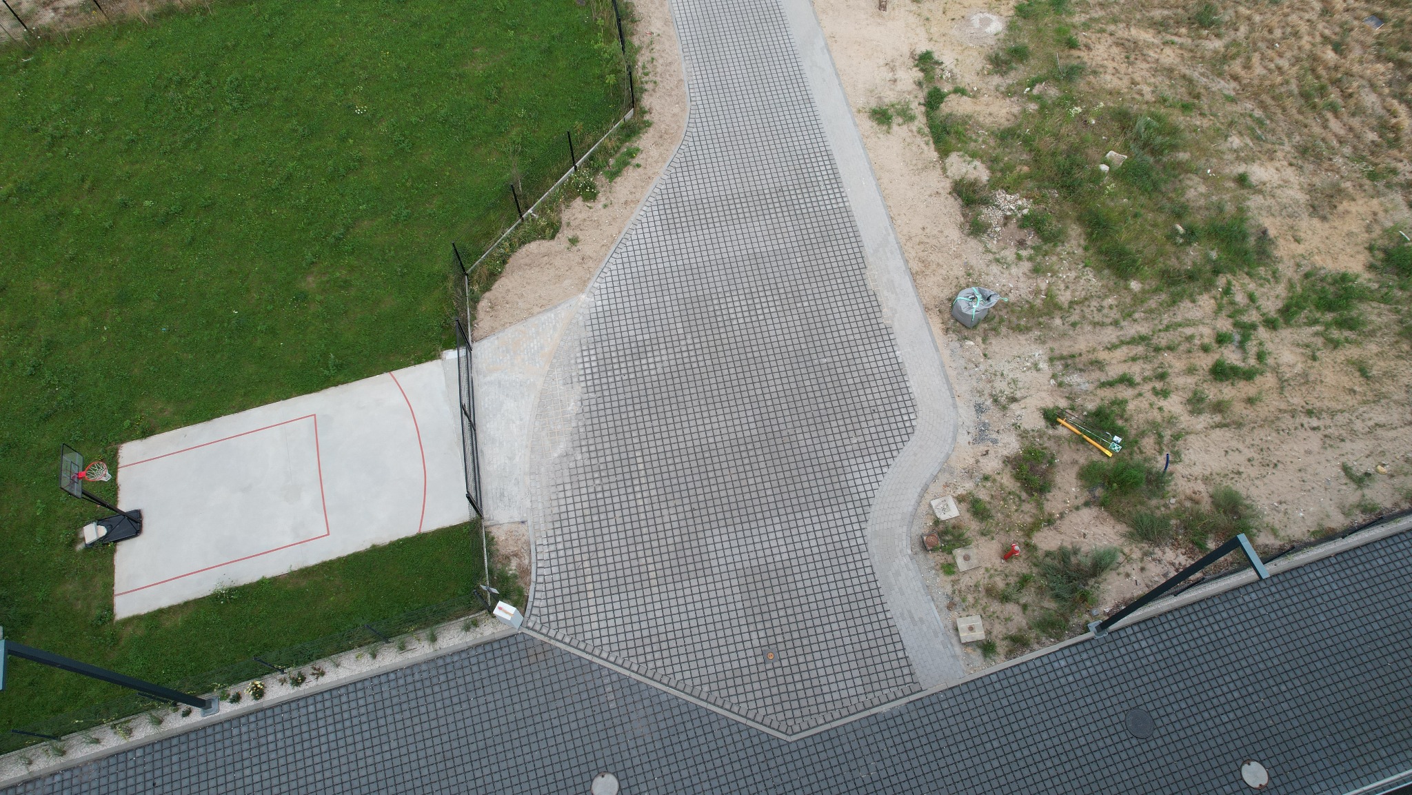 Widok z góry na ścieżkę z kostki brukowej prowadzącą do boiska, otoczoną trawnikiem i terenem z roślinnością. Kostka Ekol w Unieściu.