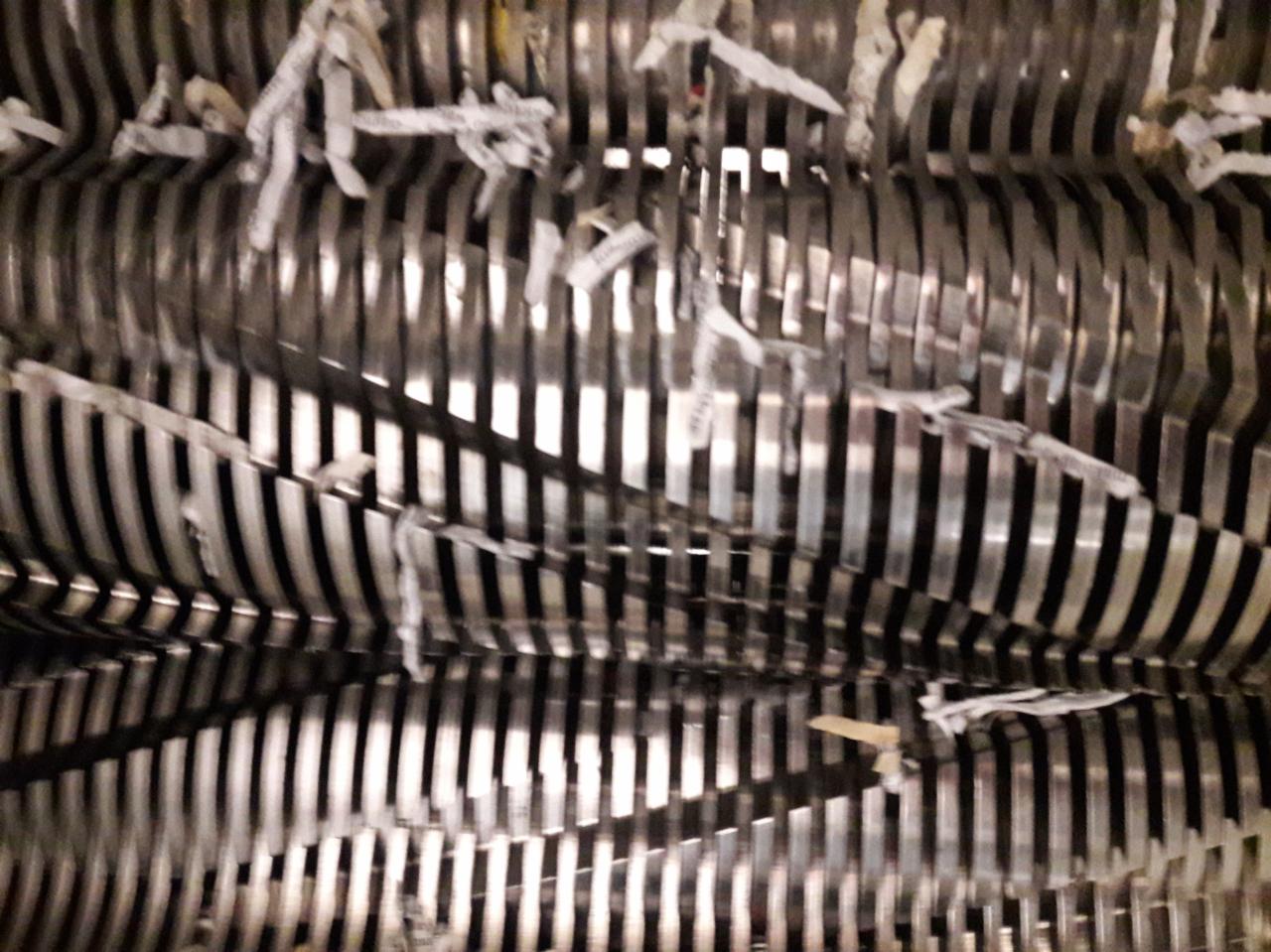 Metalowe ostrza niszczarki dokumentów z resztkami pociętego papieru pomiędzy nimi.