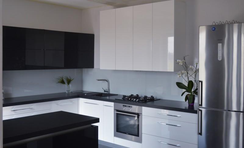 Nowoczesna kuchnia z białymi i czarnymi szafkami, stalowym zlewem, płytą gazową i piekarnikiem, uzupełniona o srebrną lodówkę i orchideę w doniczce.