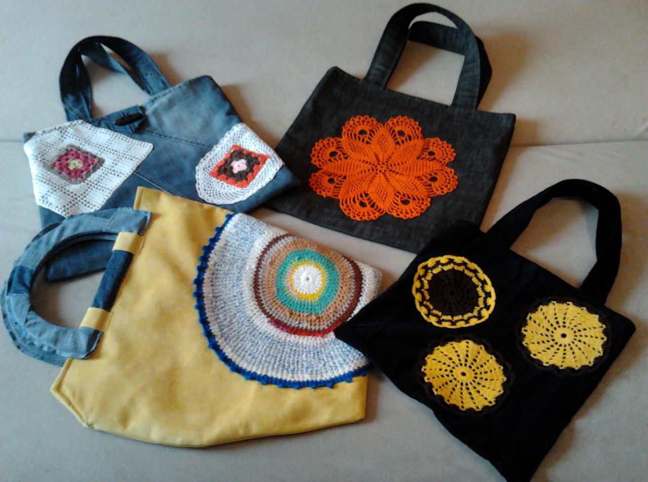 Kolekcja toreb materiałowych z aplikacjami szydełkowymi w różnych kolorach i wzorach, w tym denimowa z kwadratowymi motywami, czarna z żółtymi rozetami i żółta z półokrągłym wzorem.