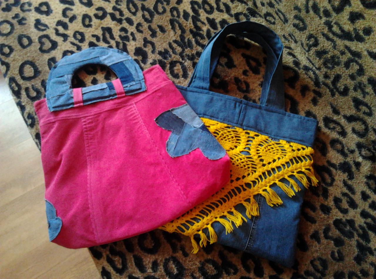 Dwie torby: różowa z denimowymi aplikacjami w kształcie serca i uchwytem, oraz dżinsowa z żółtą, ażurową wstawką z frędzlami, leżą na wzorzystej tkaninie w cętki.