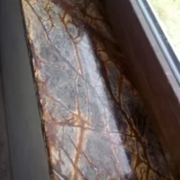 Parapet okienny z kamienia naturalnego o wzorze przypominającym korę drzewa, w odcieniach brązu i szarości, osadzony w drewnianej ramie okiennej.