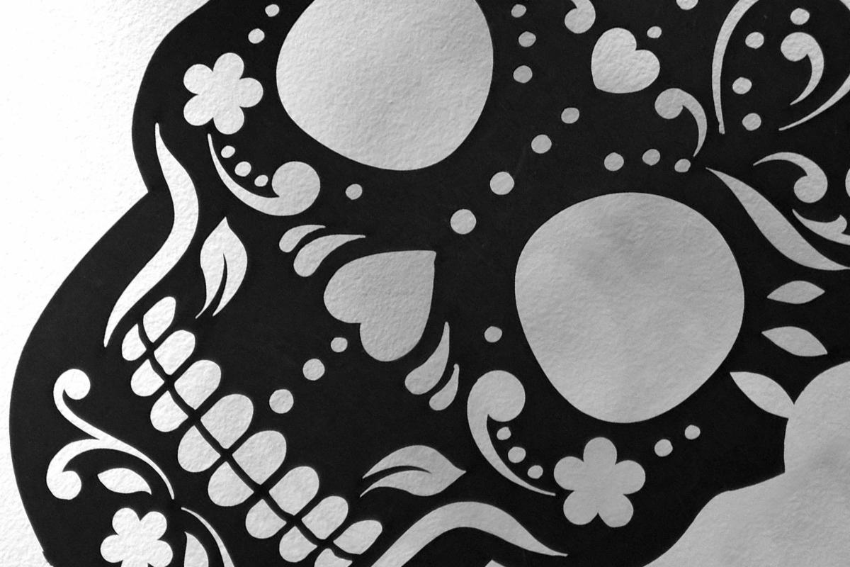 Czarno-biała grafika przedstawiająca czaszkę z ornamentami kwiatowymi, sercami i kropkami na papierze o delikatnej fakturze.