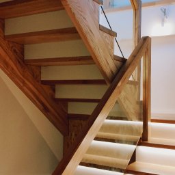 Arpex glasswood - Drewniane schody z podświetleniem LED i szklaną balustradą. Jasne drewno, nowoczesny design, ciepłe oświetlenie. Widok z dołu, podkreślający detale konstrukcji.