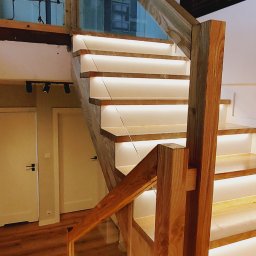 Arpex glasswood - Drewniane schody z podświetleniem LED i szklaną balustradą. Widoczne detale wykończenia i naturalna kolorystyka drewna. Ujęcie z dołu, podkreślające konstrukcję.