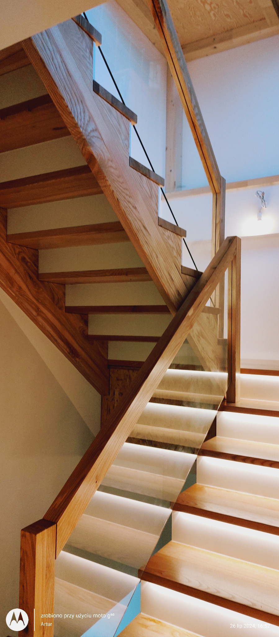 Drewniane schody z podświetleniem LED i szklaną balustradą. Jasne drewno, nowoczesny design, ciepłe oświetlenie. Widok z dołu, podkreślający detale konstrukcji.