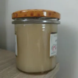 Słoik z kremowym miodem na drewnianej półce, z brązową pokrywką w plaster miodu.