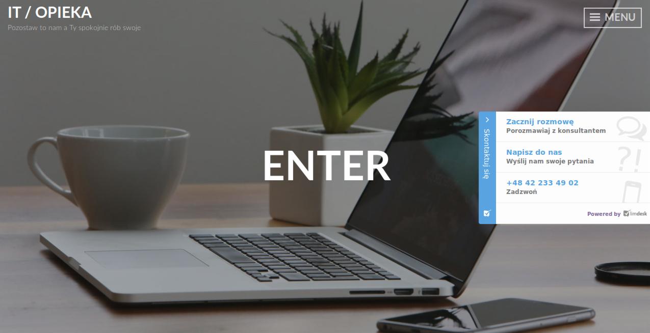 Laptop z otwartą klapą na drewnianym biurku, obok biała filiżanka, doniczka z sukulentem i smartfon; na ekranie widoczny interfejs strony internetowej z napisem 'ENTER' i menu 'Skontaktuj się'.