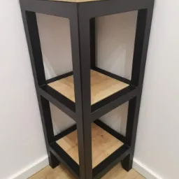 Metalowa konstrukcja regału z drewnianymi półkami w narożniku pomieszczenia, widoczne połączenia spawane.